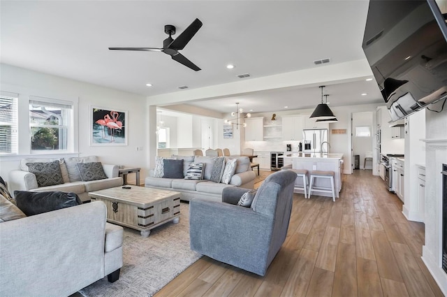 living room with wine cooler, sink, ceiling fan with notable chandelier, and light hardwood / wood-style flooring