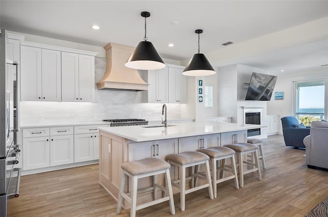 kitchen featuring sink, white cabinets, custom range hood, and an island with sink