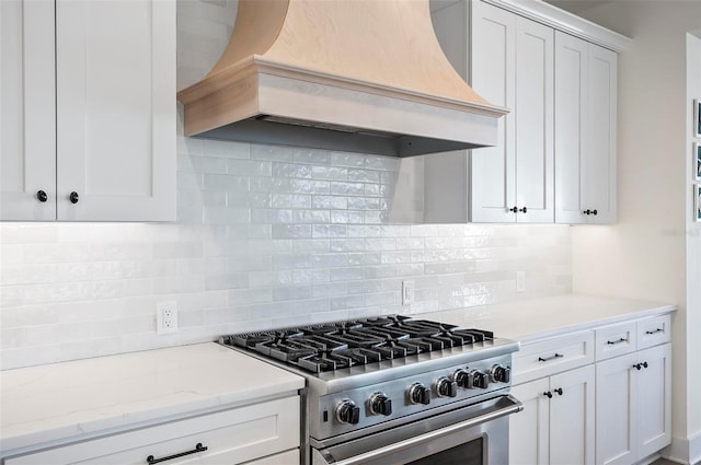 kitchen with premium range hood, white cabinetry, backsplash, light stone counters, and high end stainless steel range