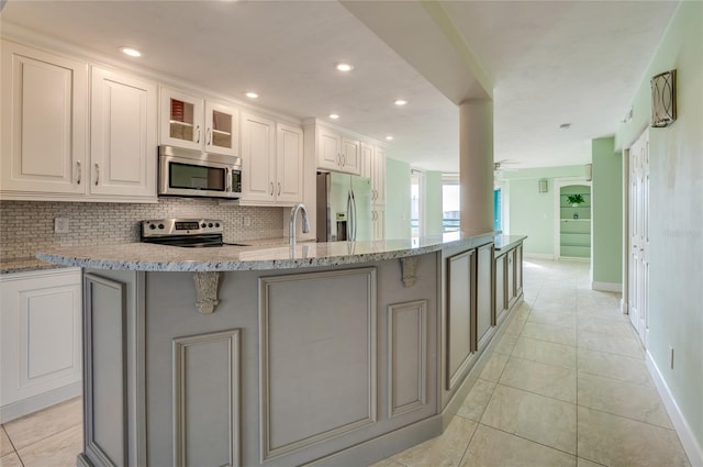 kitchen with a center island with sink, stainless steel appliances, white cabinetry, and light stone counters