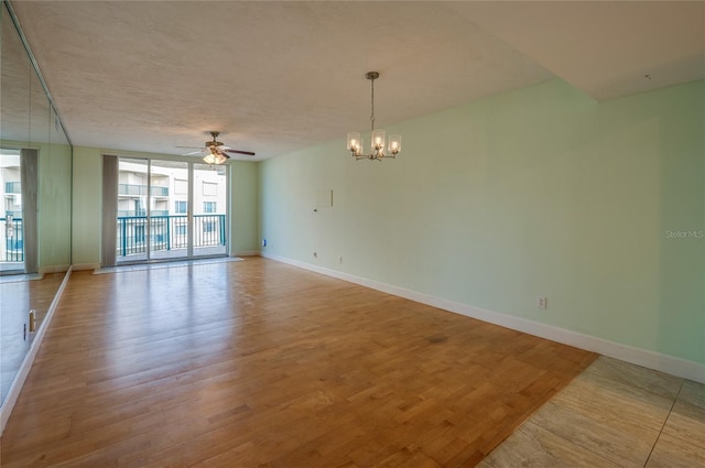 spare room with ceiling fan with notable chandelier, floor to ceiling windows, and light hardwood / wood-style flooring