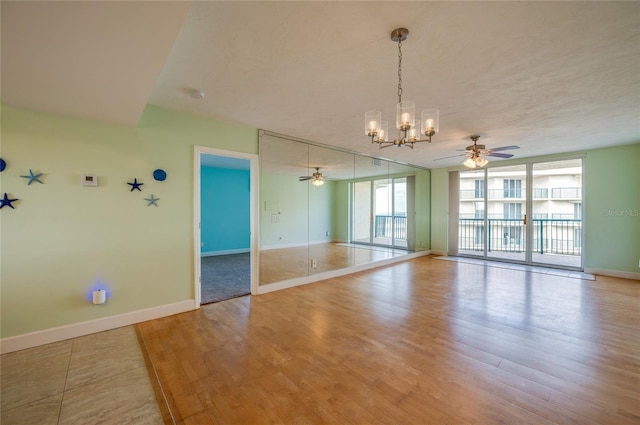 spare room with expansive windows, ceiling fan with notable chandelier, and light hardwood / wood-style floors