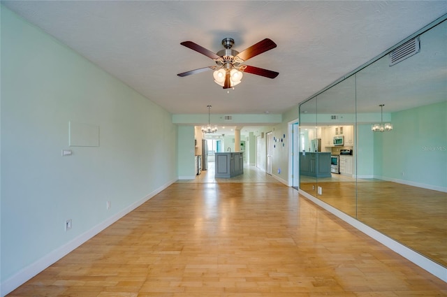 unfurnished room with ceiling fan with notable chandelier, a textured ceiling, and light hardwood / wood-style flooring