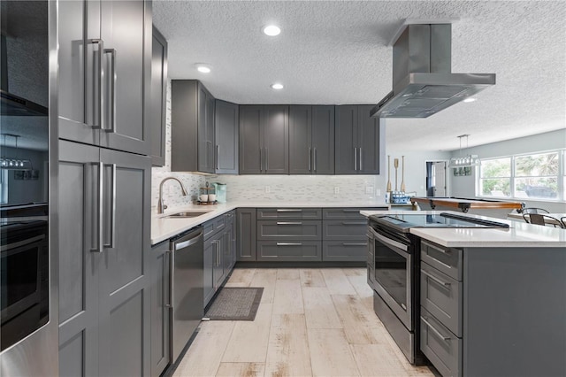 kitchen featuring appliances with stainless steel finishes, gray cabinetry, sink, island range hood, and light hardwood / wood-style flooring