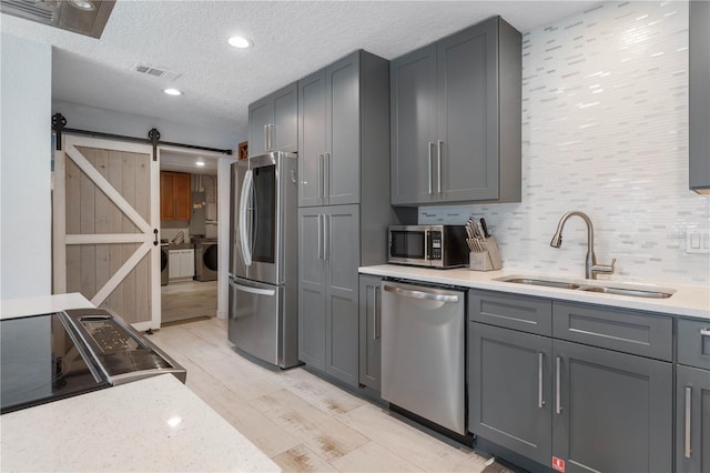 kitchen featuring a barn door, appliances with stainless steel finishes, gray cabinetry, washer and dryer, and sink