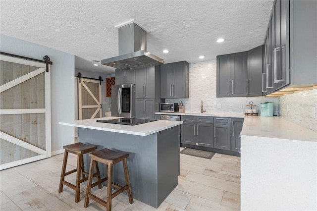 kitchen with a barn door, gray cabinets, island exhaust hood, stainless steel appliances, and a kitchen island