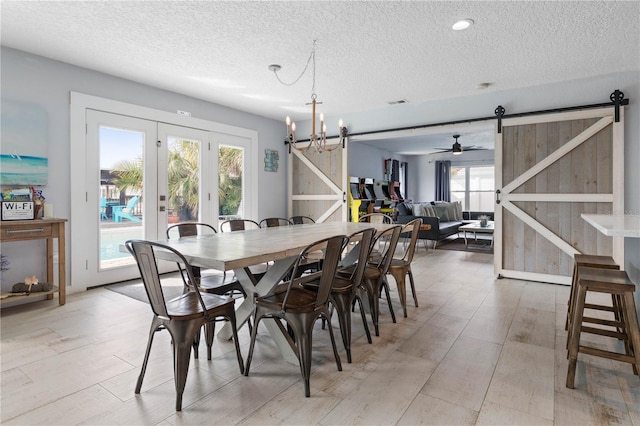 dining room with a textured ceiling, ceiling fan with notable chandelier, a barn door, and plenty of natural light