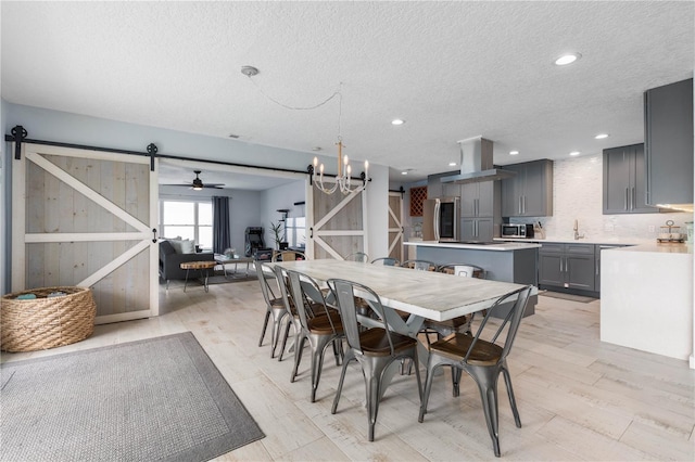 dining room with a barn door, light wood-type flooring, sink, and ceiling fan with notable chandelier