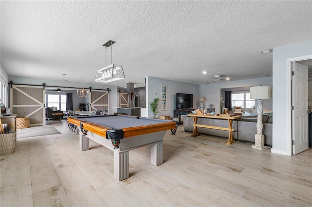 game room with light wood-type flooring, a textured ceiling, a barn door, and billiards