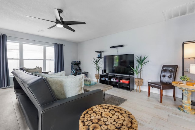 living room with a textured ceiling, ceiling fan, and light hardwood / wood-style flooring