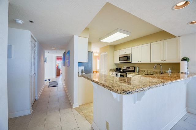 kitchen with appliances with stainless steel finishes, white cabinetry, sink, kitchen peninsula, and light tile patterned flooring