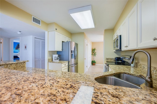 kitchen with white cabinets, appliances with stainless steel finishes, sink, and light stone counters