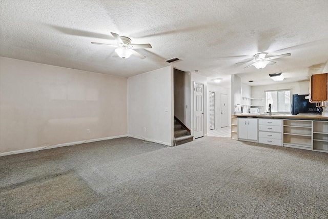 unfurnished living room with light carpet, ceiling fan, and a textured ceiling