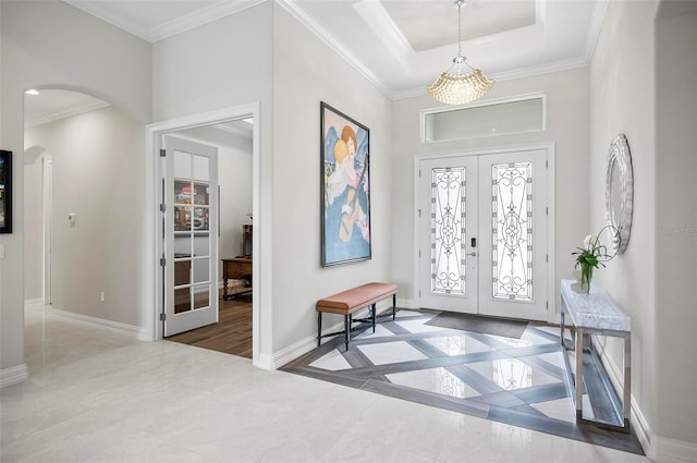 entrance foyer featuring a raised ceiling, ornamental molding, a chandelier, and french doors