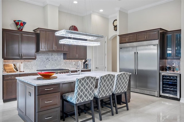 kitchen with sink, tasteful backsplash, appliances with stainless steel finishes, an island with sink, and beverage cooler