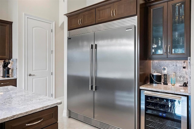 kitchen featuring built in fridge, tasteful backsplash, light stone countertops, and beverage cooler