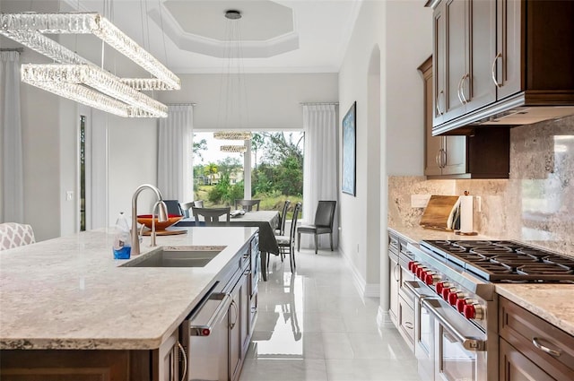 kitchen featuring sink, tasteful backsplash, appliances with stainless steel finishes, an island with sink, and a notable chandelier