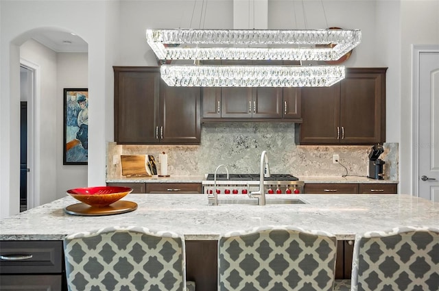 kitchen with light stone counters, dark brown cabinetry, sink, and decorative backsplash