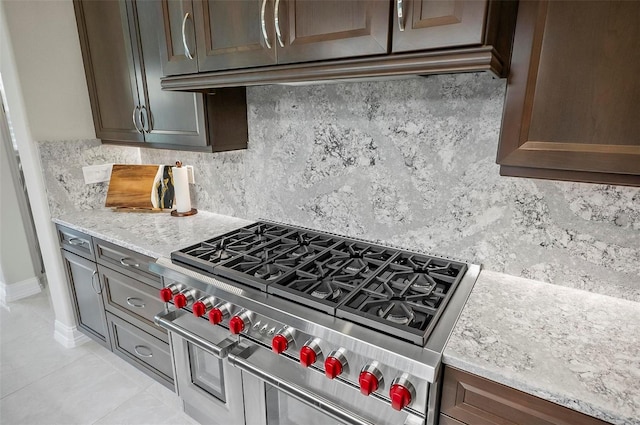 kitchen featuring light tile patterned flooring, dark brown cabinets, double oven range, light stone countertops, and backsplash