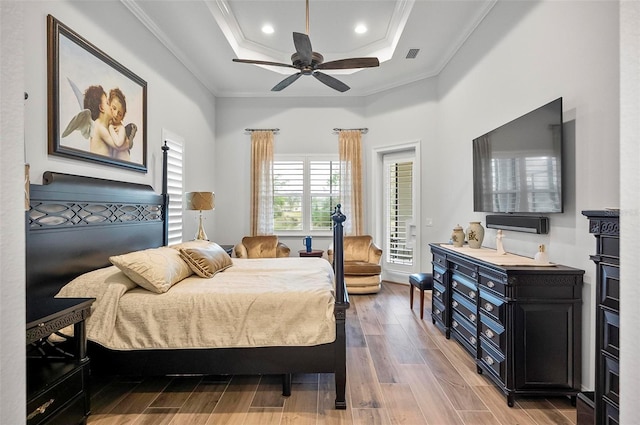 bedroom featuring crown molding, ceiling fan, wood-type flooring, and a tray ceiling