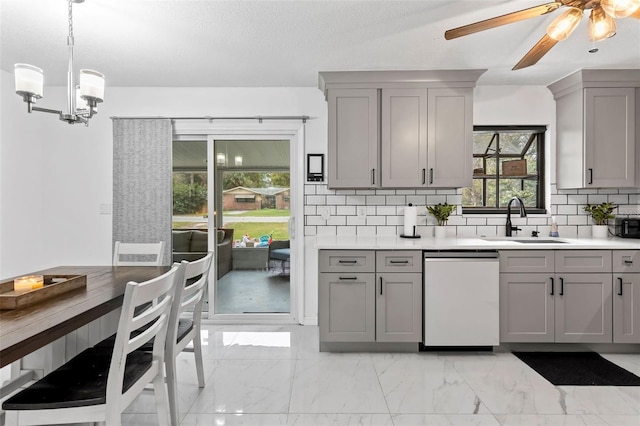 kitchen featuring hanging light fixtures, dishwashing machine, gray cabinetry, ceiling fan with notable chandelier, and sink