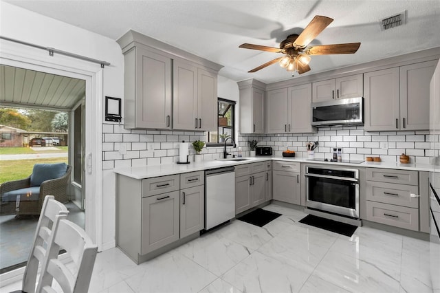 kitchen with sink, a textured ceiling, ceiling fan, gray cabinets, and appliances with stainless steel finishes