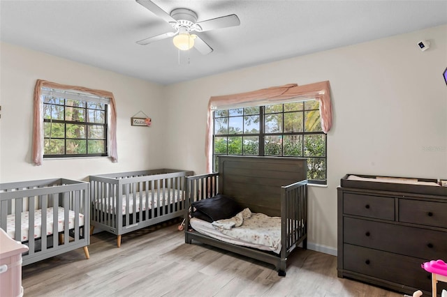 bedroom featuring a crib, ceiling fan, and light hardwood / wood-style floors