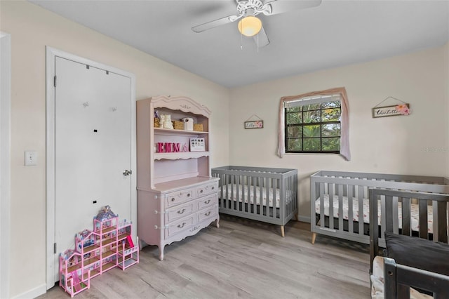 bedroom featuring a nursery area, ceiling fan, and light hardwood / wood-style flooring