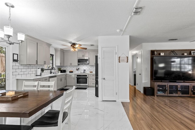 kitchen featuring gray cabinets, appliances with stainless steel finishes, sink, decorative light fixtures, and tasteful backsplash