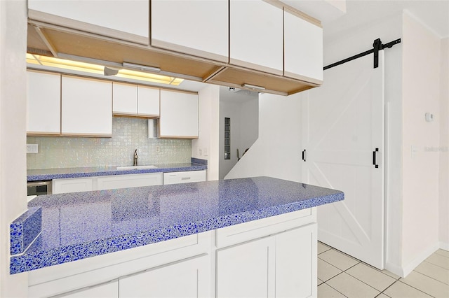 kitchen with white cabinetry, a barn door, sink, and backsplash