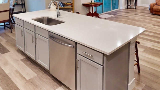 kitchen featuring sink, a center island with sink, stainless steel dishwasher, a kitchen breakfast bar, and gray cabinets