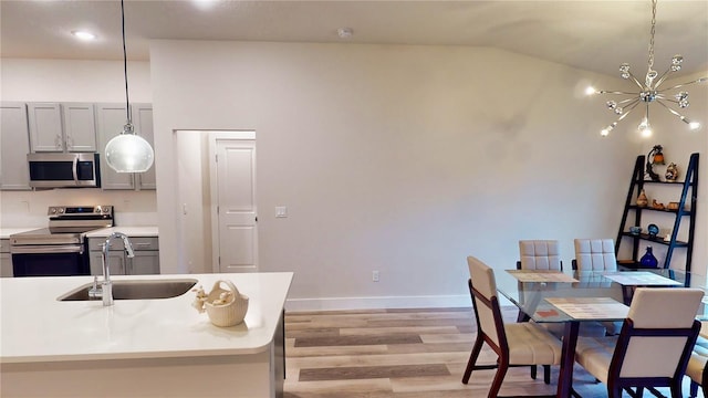 kitchen with pendant lighting, stainless steel appliances, vaulted ceiling, and sink