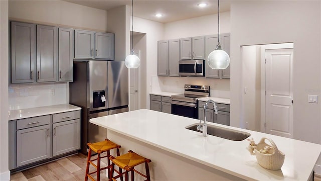 kitchen featuring sink, a breakfast bar area, gray cabinets, pendant lighting, and stainless steel appliances