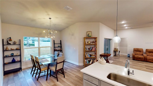 dining area with lofted ceiling, sink, light hardwood / wood-style flooring, and a chandelier