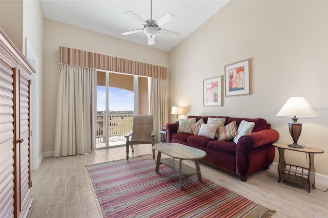 living room with a towering ceiling, ceiling fan, and light wood-type flooring