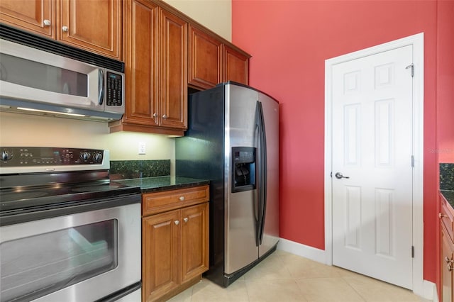 kitchen featuring light tile patterned flooring, stainless steel appliances, and dark stone countertops