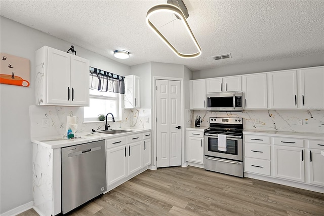 kitchen with appliances with stainless steel finishes, white cabinetry, backsplash, and sink