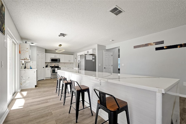 kitchen featuring light stone counters, stainless steel appliances, a kitchen bar, backsplash, and white cabinetry