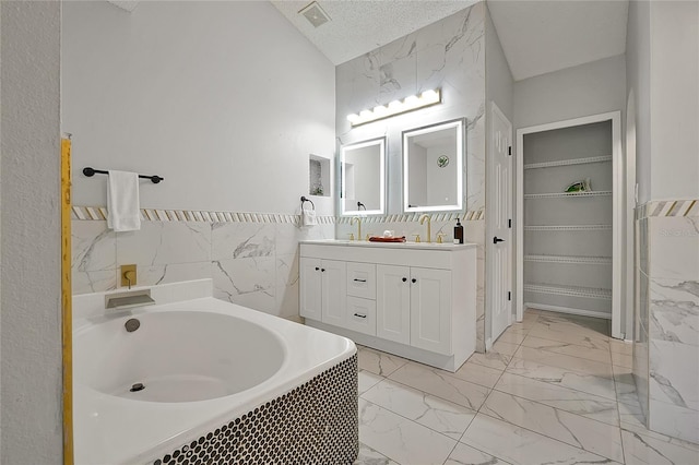 bathroom featuring a washtub, a textured ceiling, tile walls, lofted ceiling, and vanity