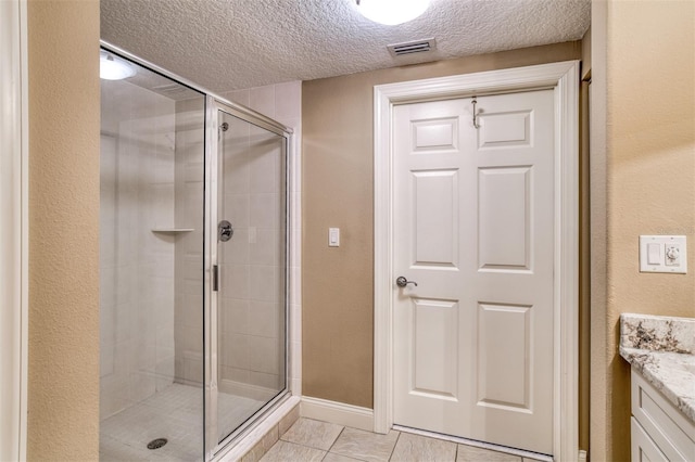 bathroom with tile patterned flooring, vanity, a textured ceiling, and a shower with shower door