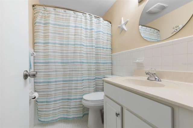 bathroom with toilet, vanity, and tile walls