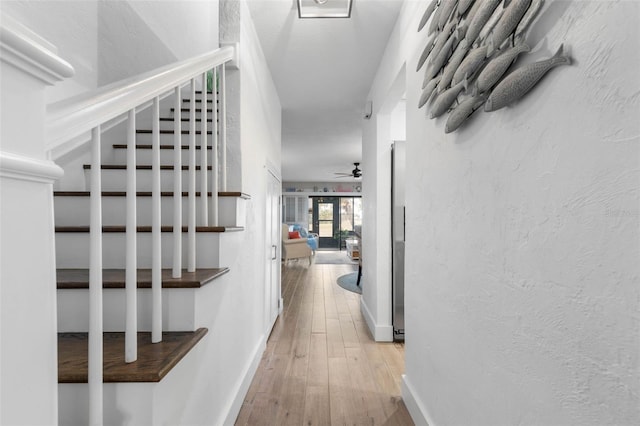 corridor featuring light wood finished floors, stairs, baseboards, and a textured wall