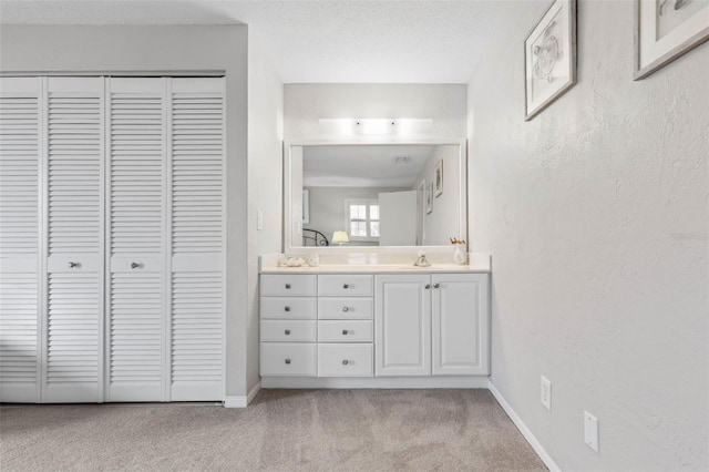 bathroom with a closet, a textured wall, vanity, a textured ceiling, and baseboards