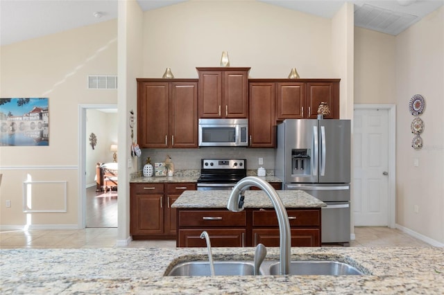 kitchen with high vaulted ceiling, light stone countertops, sink, and stainless steel appliances