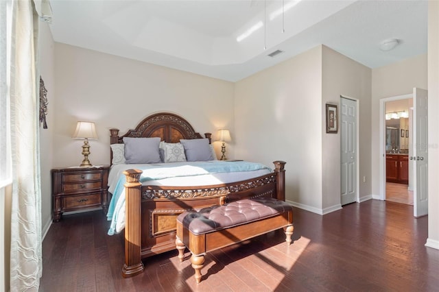 bedroom featuring a raised ceiling, dark hardwood / wood-style floors, and ensuite bathroom