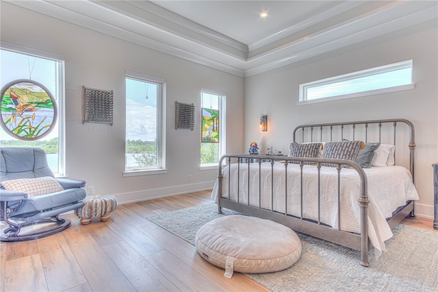 bedroom featuring a tray ceiling, ornamental molding, and light wood-type flooring