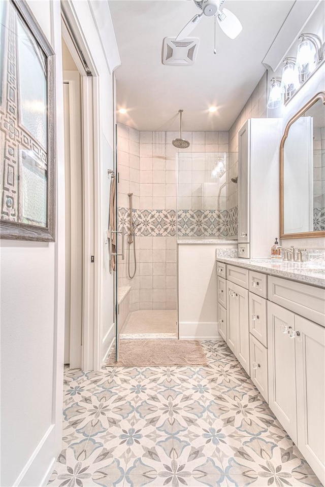 bathroom featuring ceiling fan, tiled shower, vanity, and tile patterned flooring