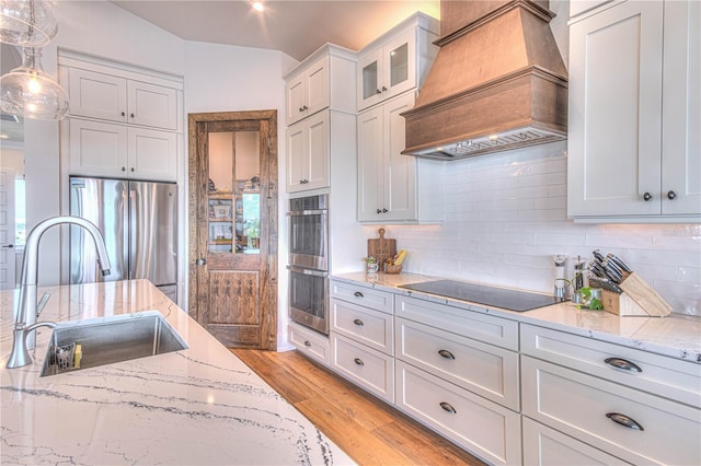 kitchen with premium range hood, sink, white cabinetry, hanging light fixtures, and stainless steel appliances