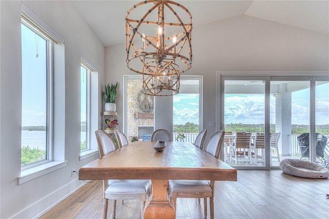 dining room featuring lofted ceiling, light wood-type flooring, a healthy amount of sunlight, and an inviting chandelier