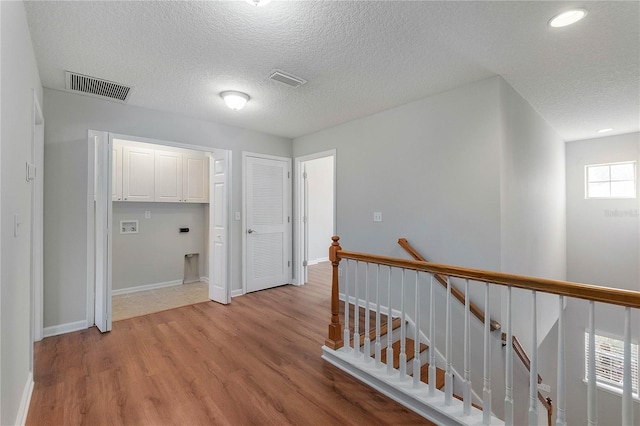 hallway with a textured ceiling and light hardwood / wood-style flooring